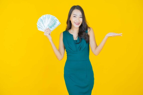 Asiatische Frau die die linke Hand wie eine Waagschale zur Seite streckt und in der rechten Hand gefächerte Geldscheine hält