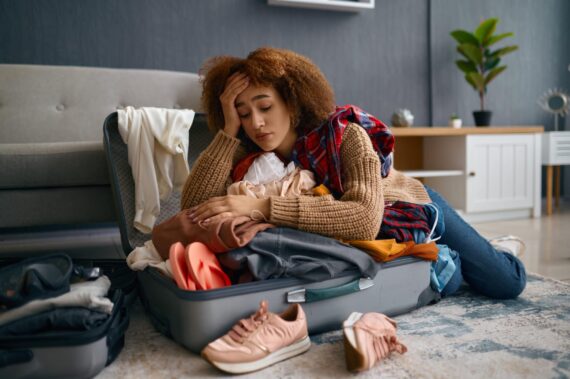 Eine traurige Frau sitzt auf dem Boden und beugt sich über ihren teilweise ausgepackten Koffer